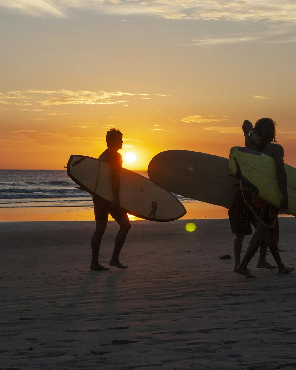 Surfers walking along the beach with their boards at sunset